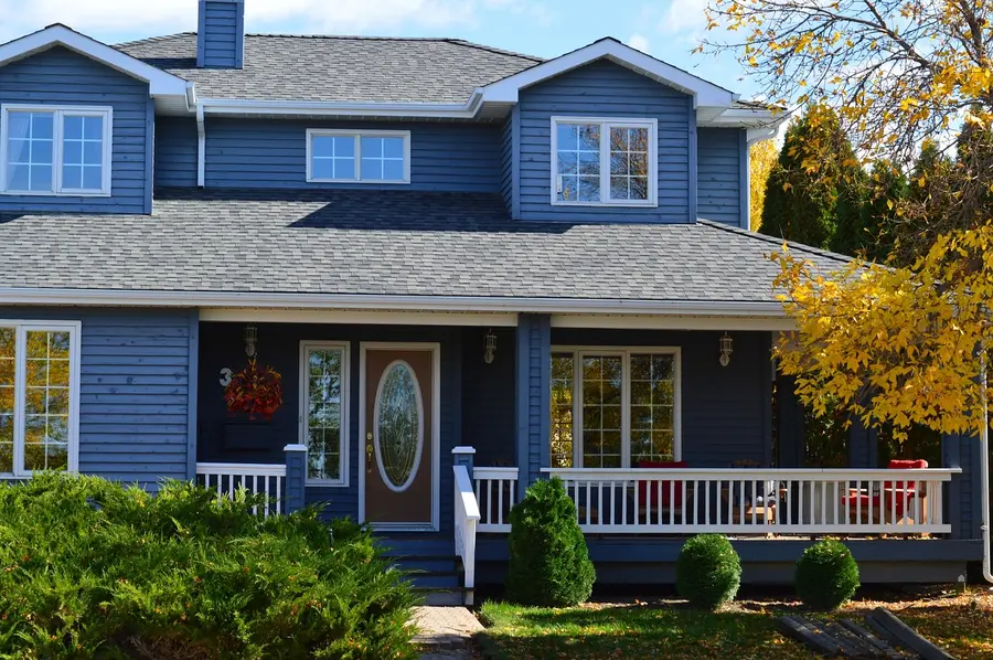 Two-story Kentucky-style home with a yellow tree dropping leaves in fall